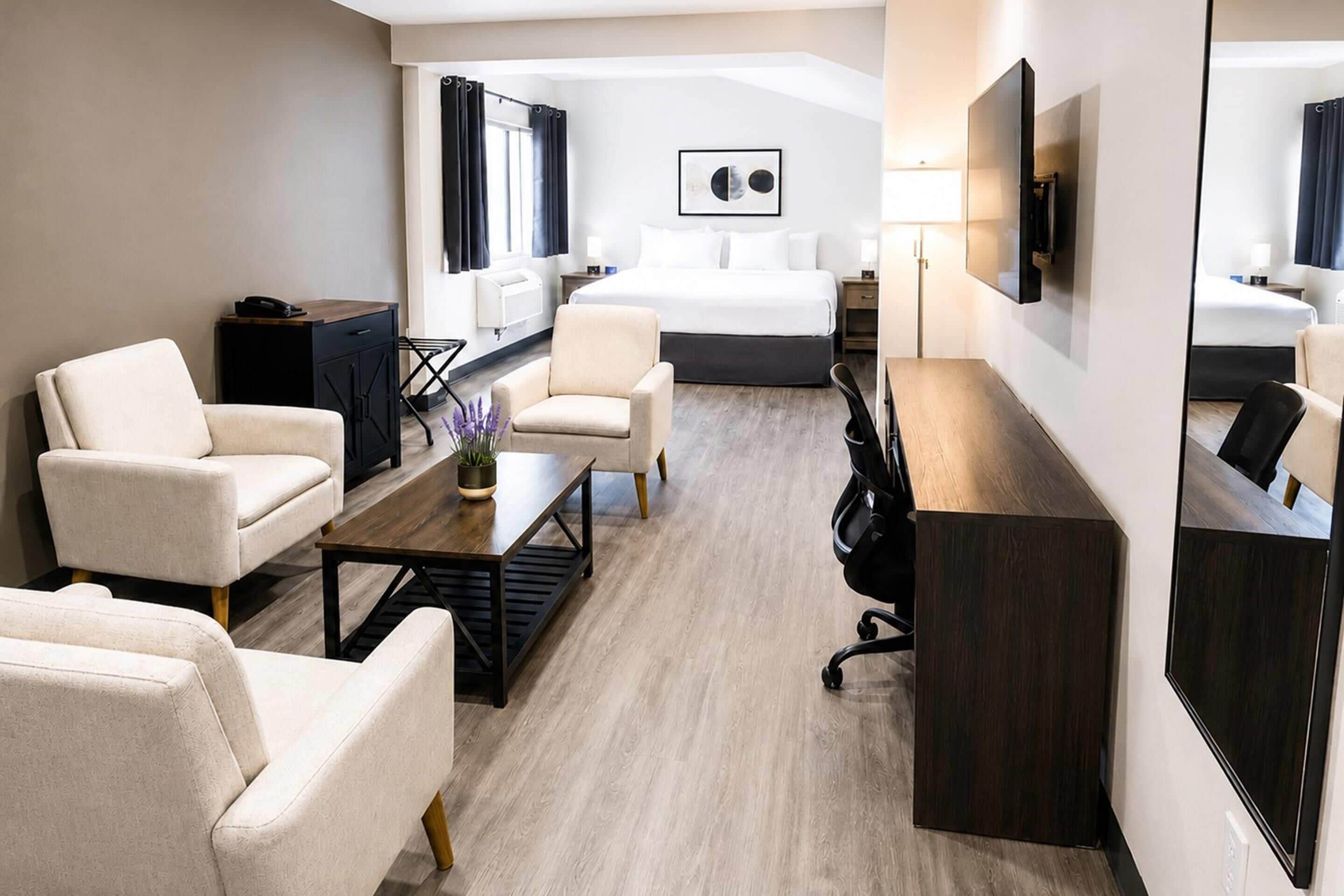 Moderni hotellihuone, jossa on sänky, kaksi nojatuolia, työpöytä, sohvapöytä ja televisio.
