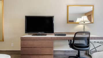 A hotel room with a flat-screen TV, a desk with drawers, a chair, and a lamp.