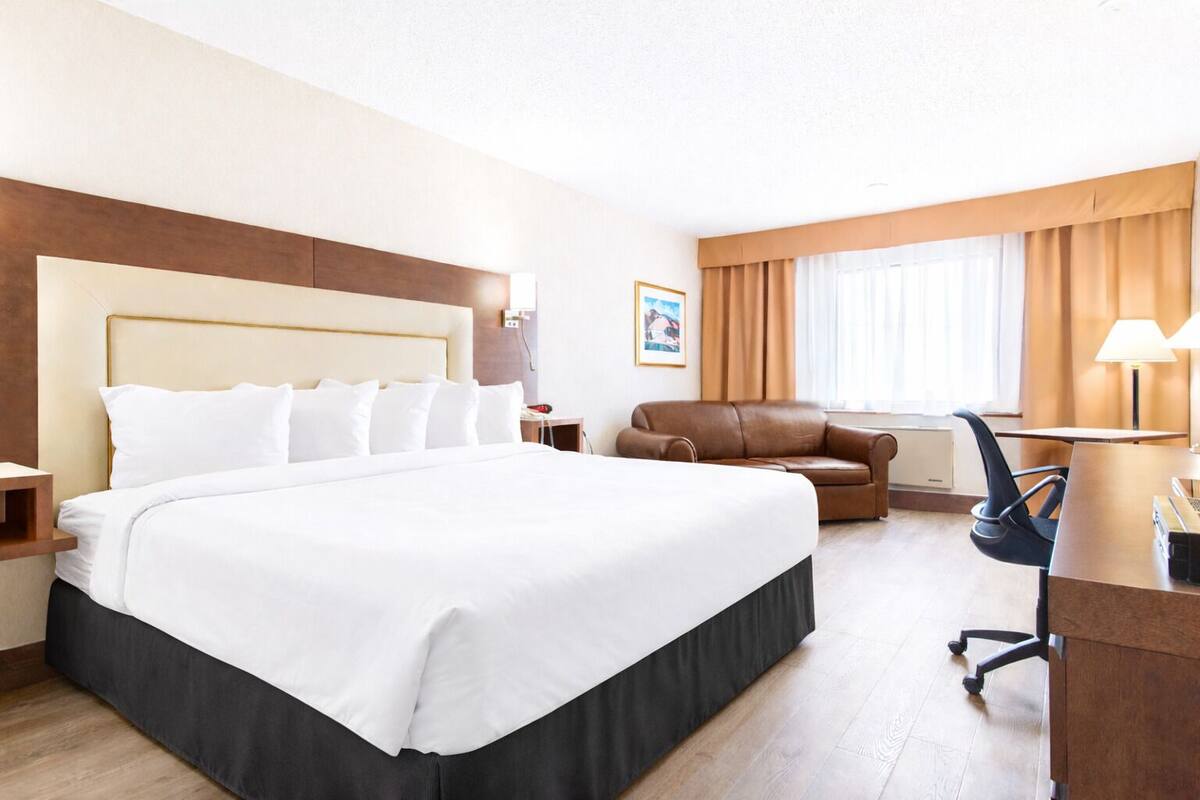 Une chambre d’hôtel avec un grand lit, un canapé, un bureau avec une chaise et une fenêtre avec des rideaux.