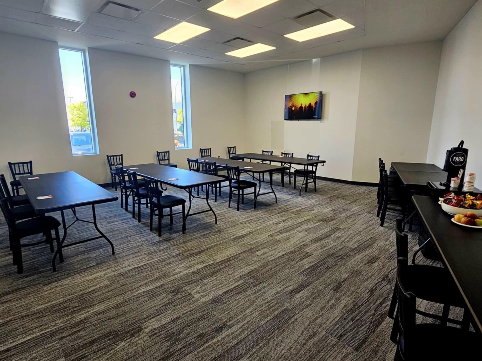 A conference room with multiple tables and chairs, large windows, and a painting on the wall.