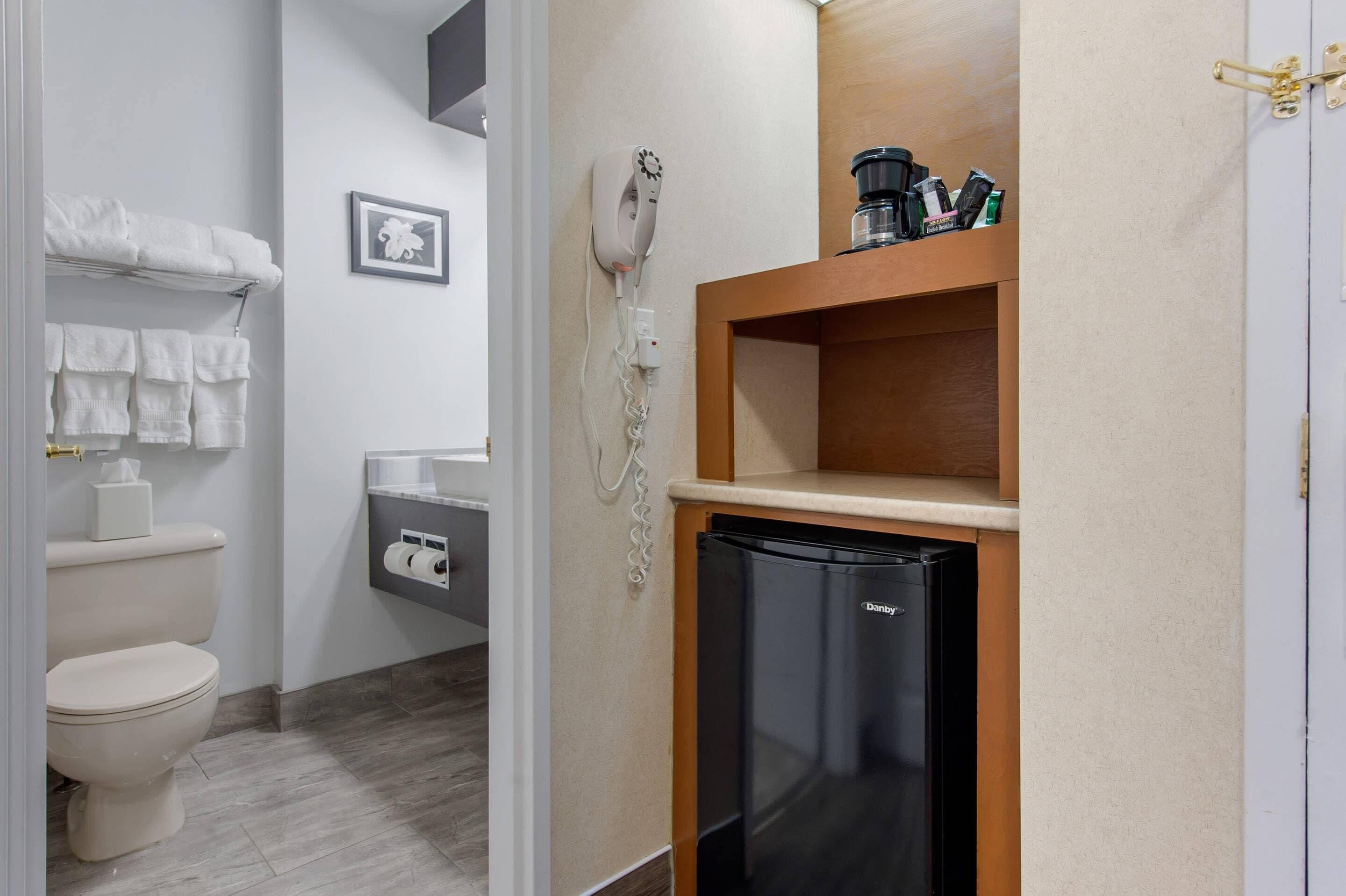 Casa de banho compacta com sanita, porta-toalhas e pequeno frigorífico.
