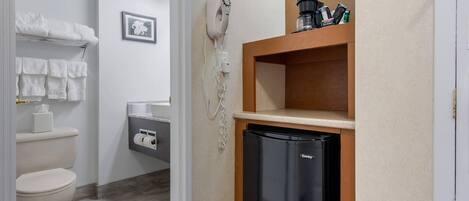 A compact bathroom with a toilet, towel rack, and a small refrigerator.