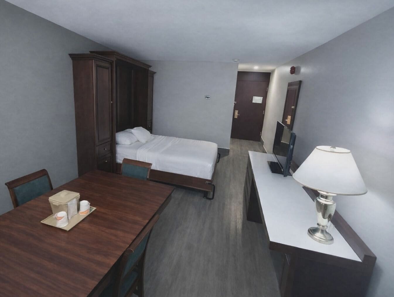 Een hotelkamer met een houten bureau, een bed, een kast, een televisie en een lamp.