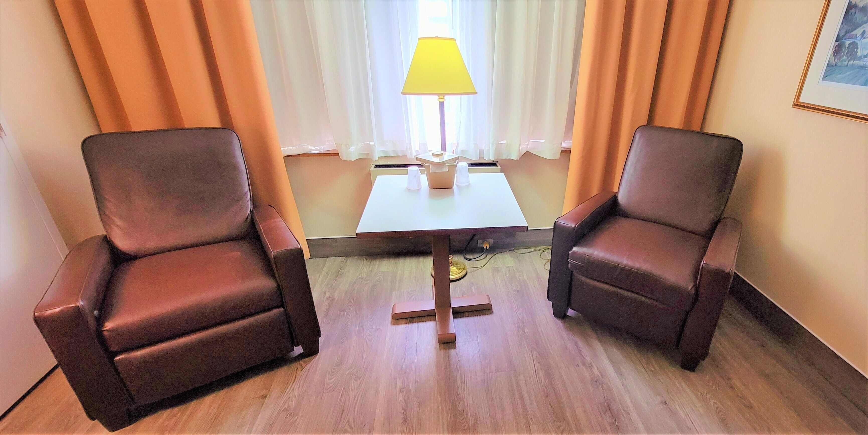 A hotel room with two leather armchairs, a small table with a lamp, and a window with curtains.