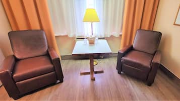Una habitación de hotel con dos sillones de cuero, una mesita con lámpara y un ventanal con cortinas.