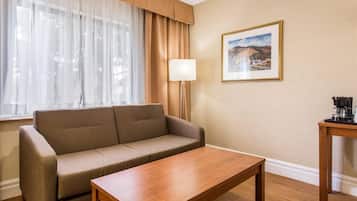 A room with a sofa, a wooden table, a lamp, a framed picture on the wall, and a coffee machine on a small table.