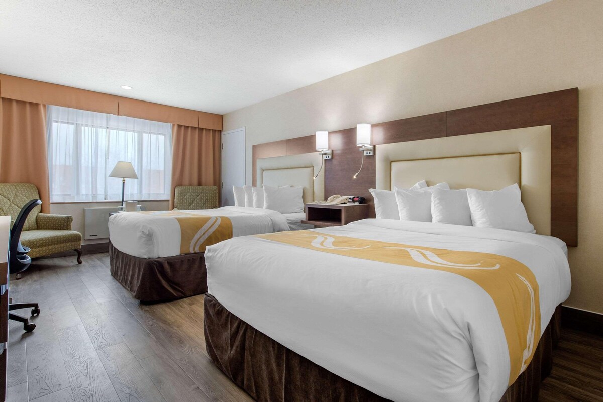 Habitación de hotel con dos camas, un escritorio, una silla, una lámpara y una ventana con cortinas.