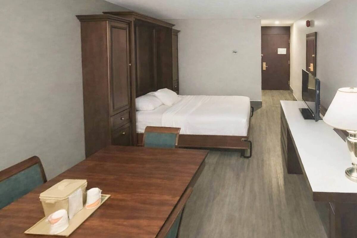 Une chambre d’hôtel comprenant un lit, une armoire en bois, un bureau avec une lampe et un téléviseur.