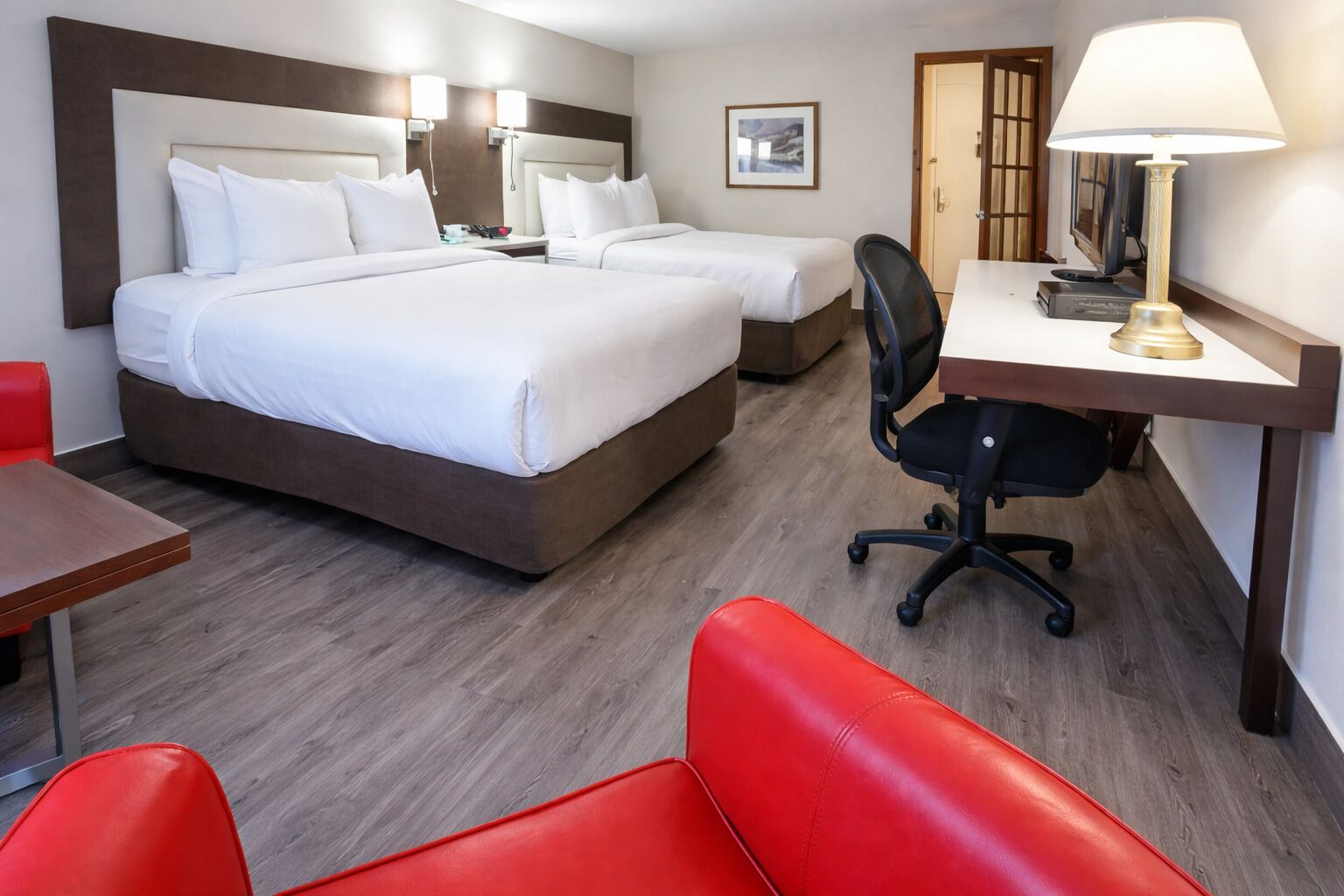 A hotel room with two beds, a desk, a chair, and a TV.