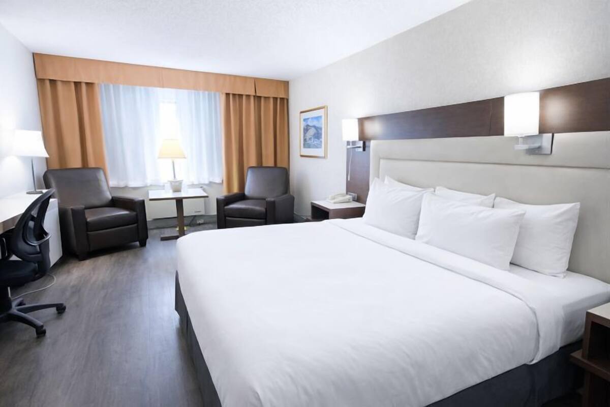 Une chambre d’hôtel avec un grand lit, deux fauteuils, un bureau, une lampe et une table de chevet avec un téléphone.