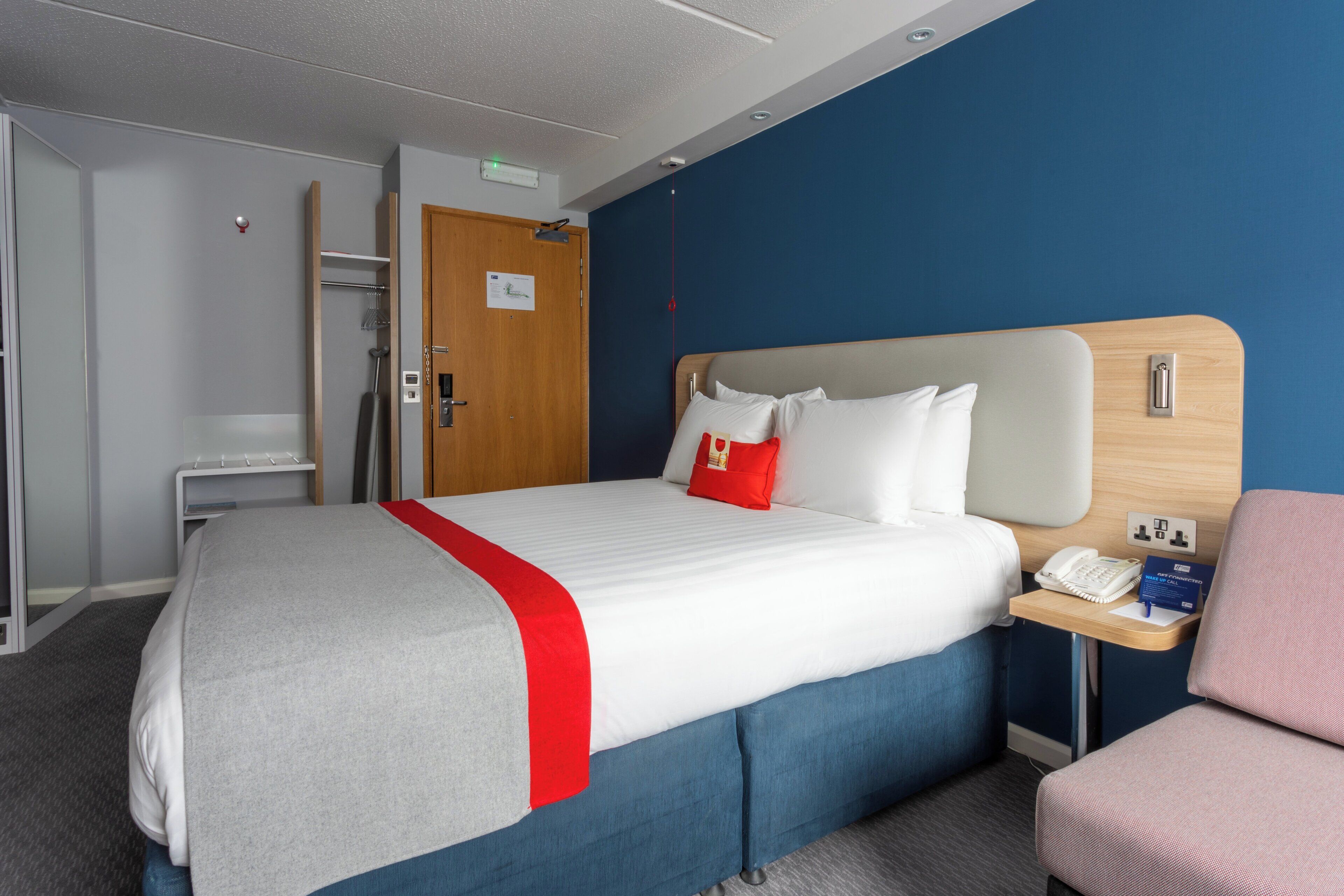 Habitación de hotel con cama, mesita de noche con teléfono, una silla y puerta que da a un baño.