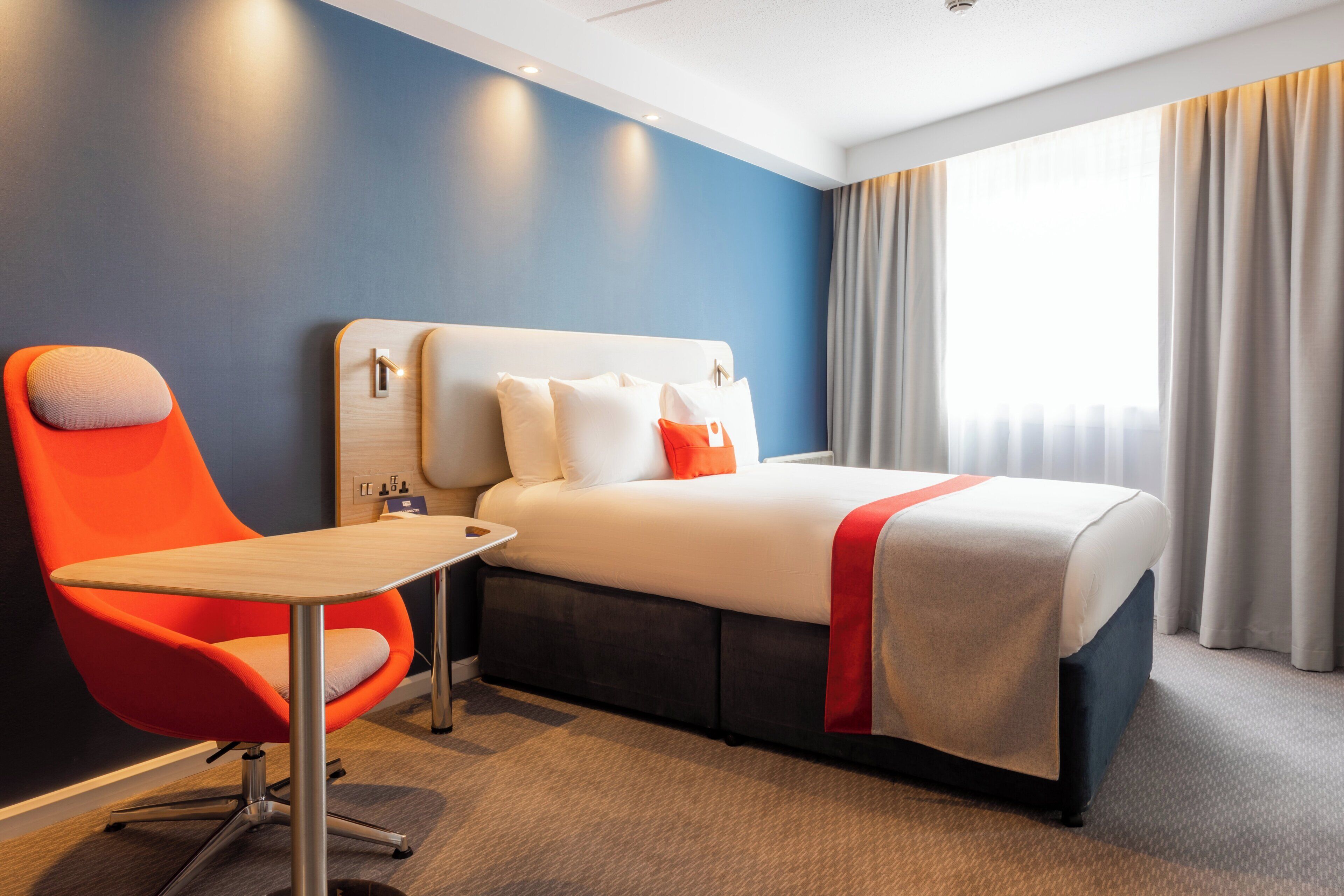 A hotel room with a bed, a desk, a chair, and a window with curtains.