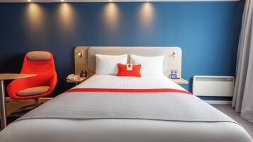 A hotel room with a large bed, a red chair, a bedside table with a phone, and a nightstand with a lamp.