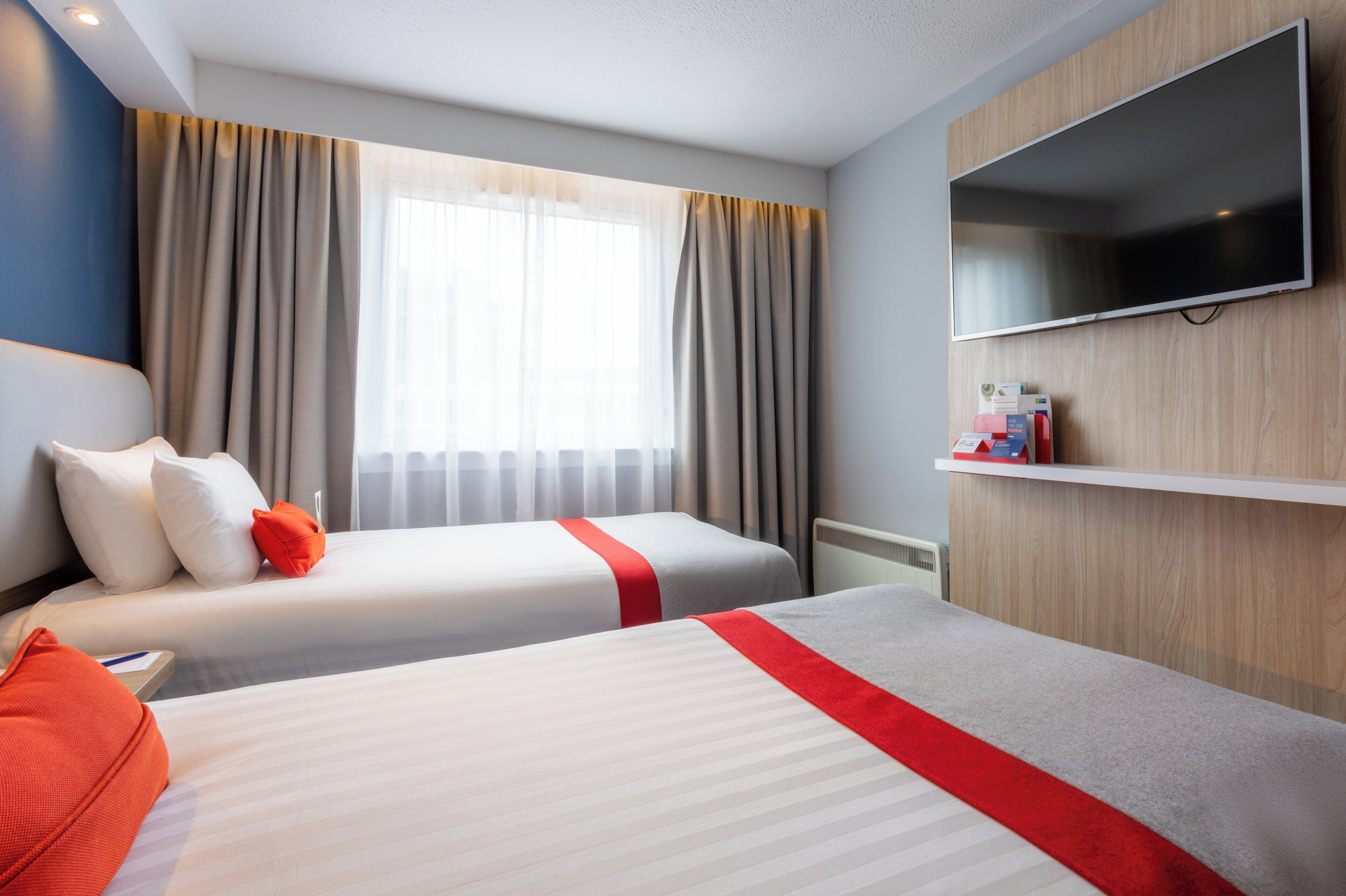A hotel room with two beds, a TV, and a window with curtains.