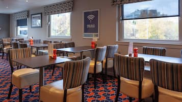 A hotel dining area with striped upholstered chairs, tables, and a patterned carpet.