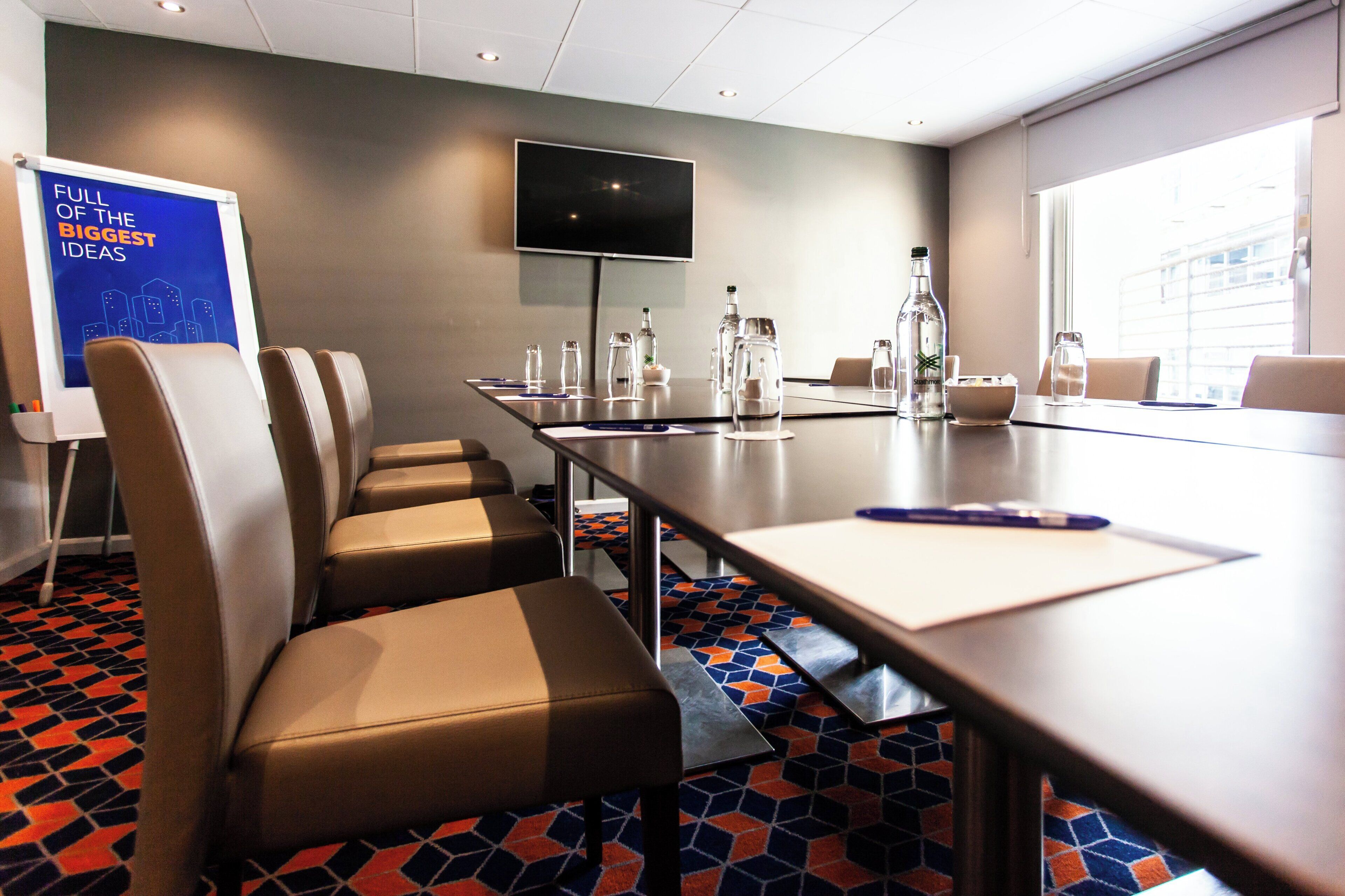 A conference room with a long table, chairs, a whiteboard, and a television on the wall.