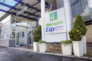 A Holiday Inn Express sign with a glass entrance and two potted plants. - Holiday Inn Express Glasgow City Theatreland by IHG (Glasgow)