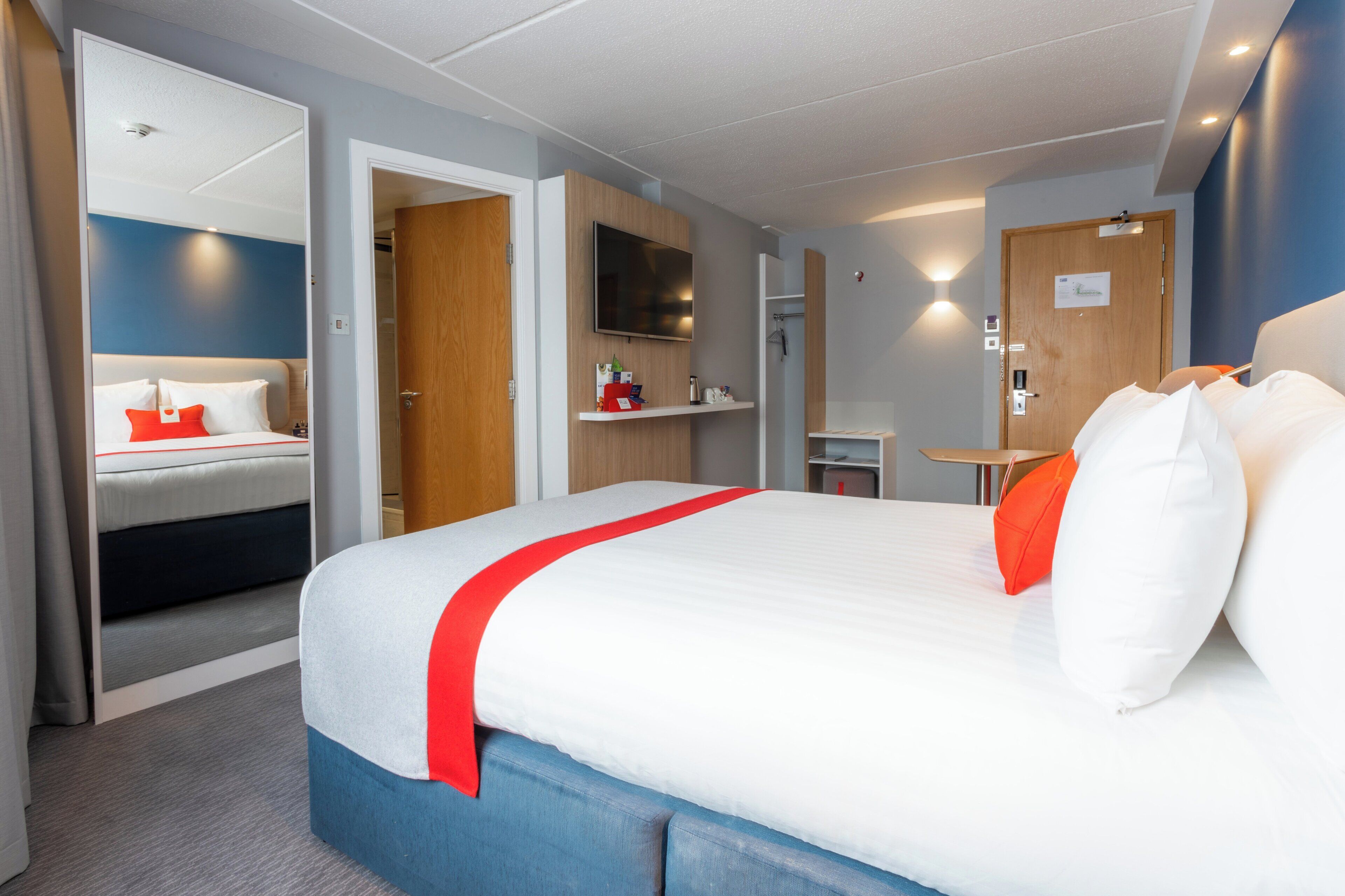 A hotel room with a bed, a TV, a desk, and a shower area.