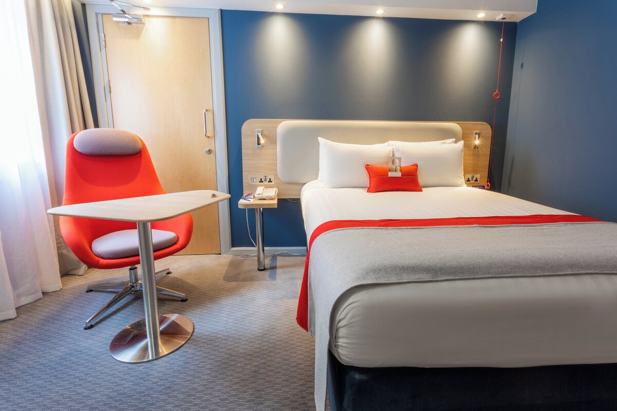 A hotel room with a bed, a desk, a chair, and a nightstand.