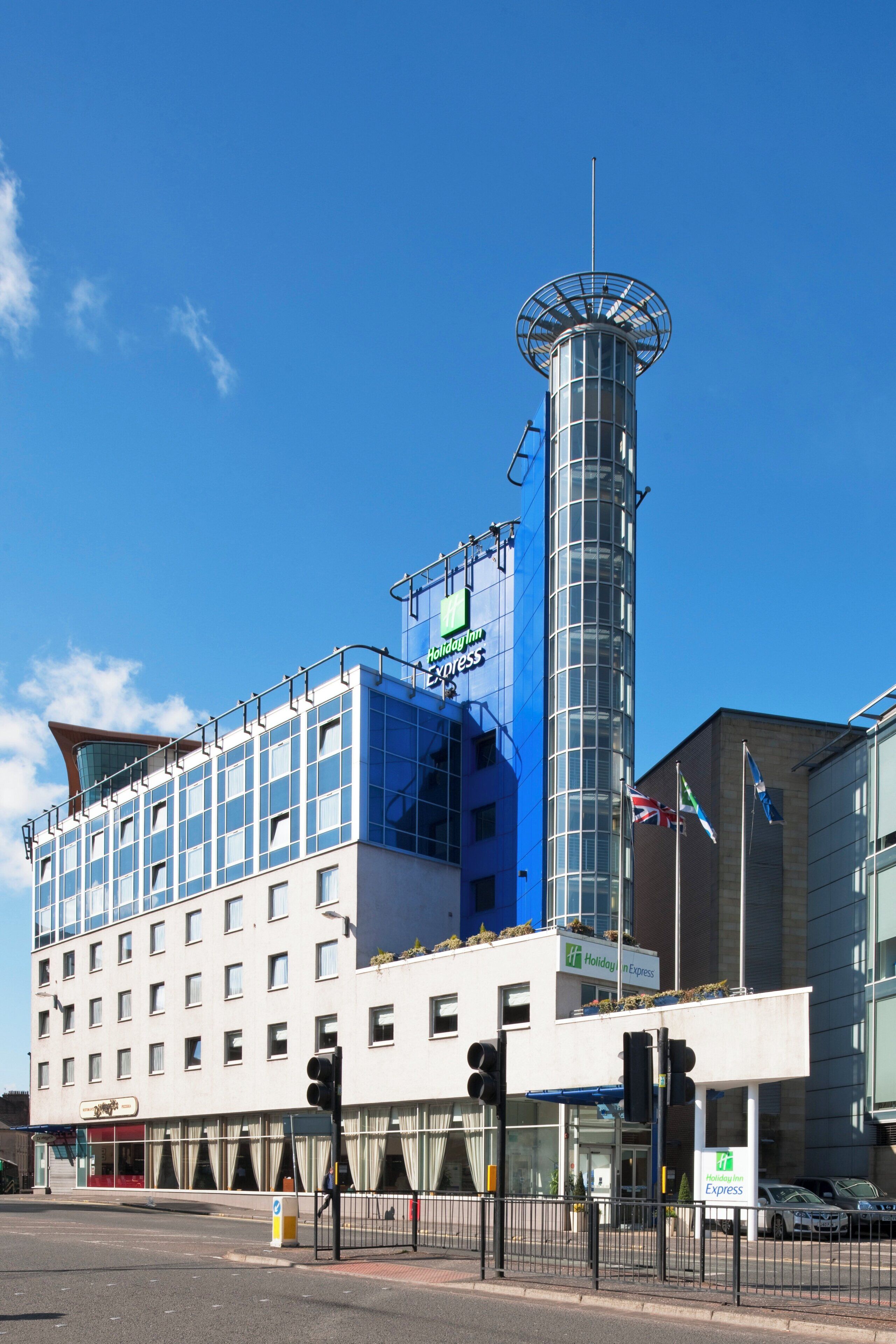 Un hotel Holiday Inn Express con una torre cilíndrica, numerosas ventanas y un cielo azul despejado.