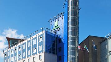Un hotel Holiday Inn Express con una torre cilíndrica, numerosas ventanas y un cielo azul despejado.