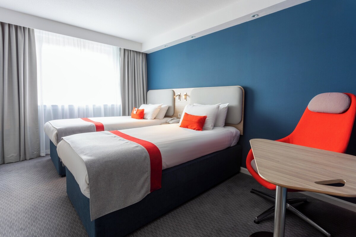 A hotel room with two beds, a desk, and a chair.