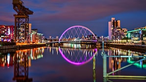 A nighttime cityscape with a prominent bridge reflecting on calm water, surrounded by illuminated buildings. - Holiday Inn Express Glasgow City Theatreland by IHG (Glasgow)