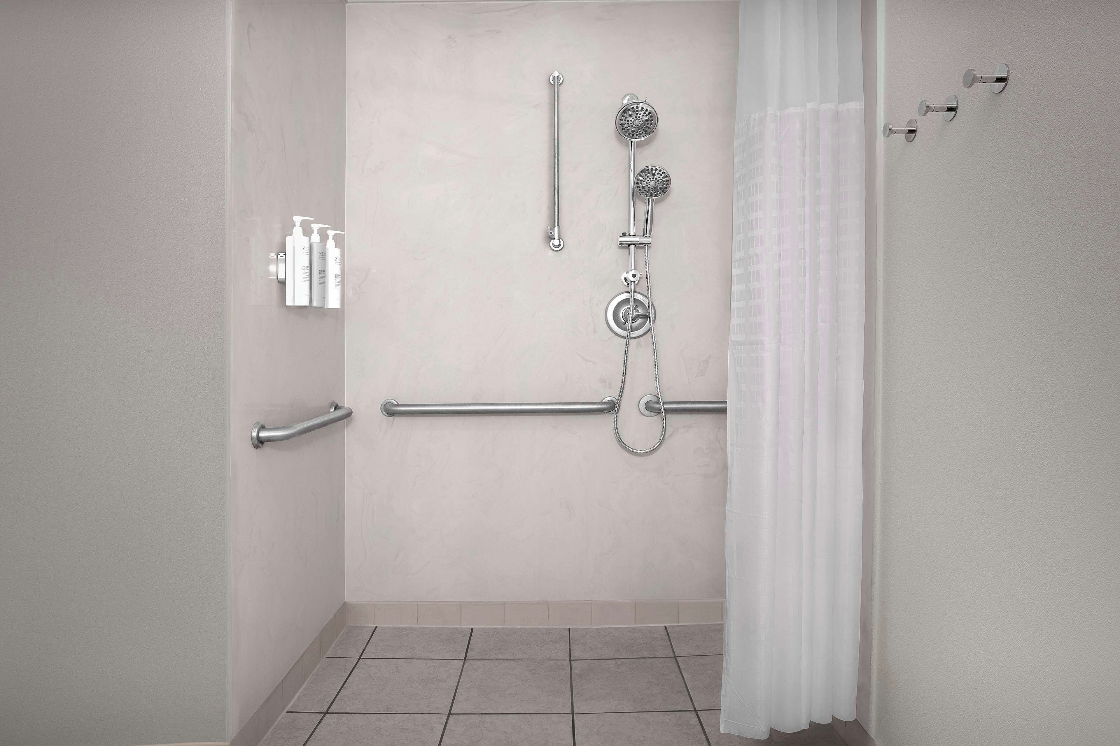 A shower area with a grab bar, handheld showerhead, and a wall-mounted faucet.