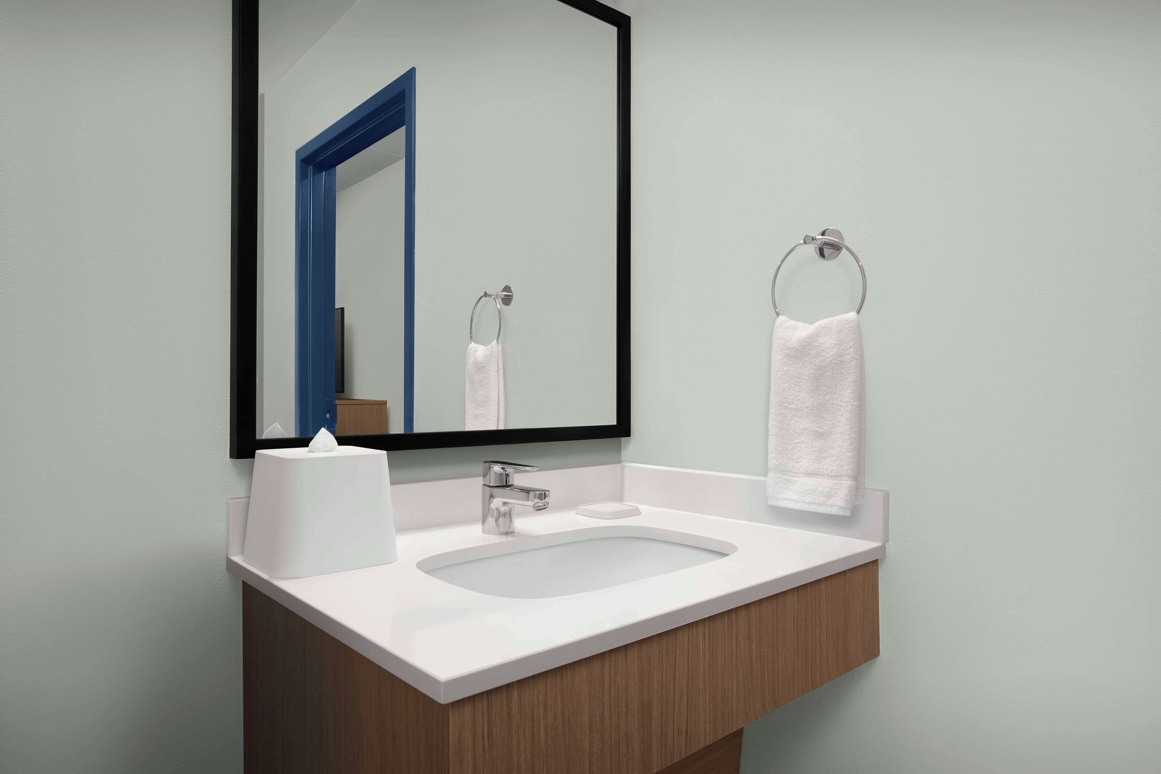 A modern bathroom with a white sink, a mirror with a black frame, and a towel rack with a white towel.