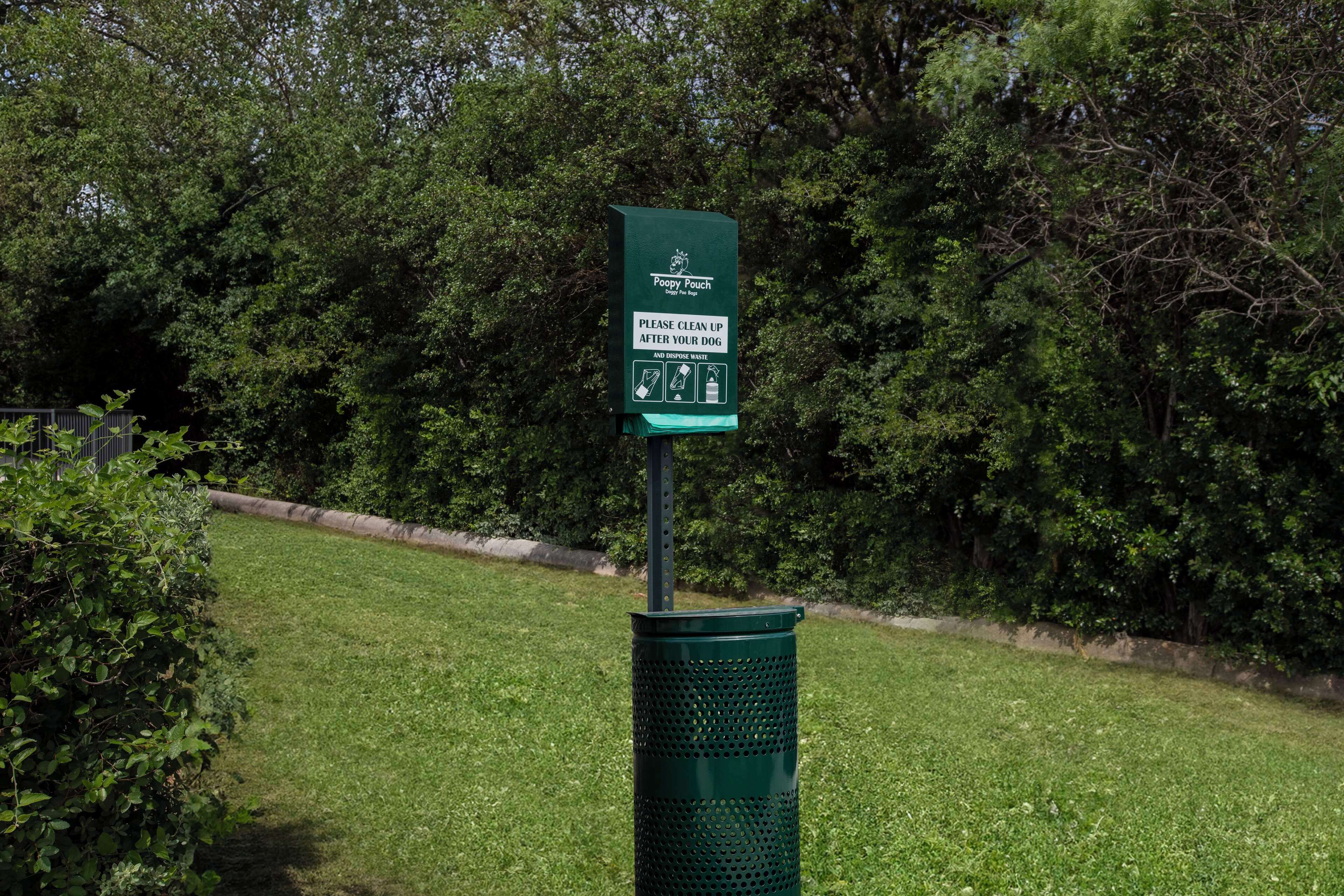A green trash can with a sign that instructs dog owners to clean up after their pets and dispose of waste properly.