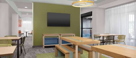 Un salón de conferencias moderno con mesas y bancos de madera, un televisor de pantalla plana grande y una pared de acento verde.
