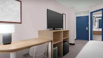 A modern hotel room with a wooden desk, a television, a chair, a trash bin, and a blue door.