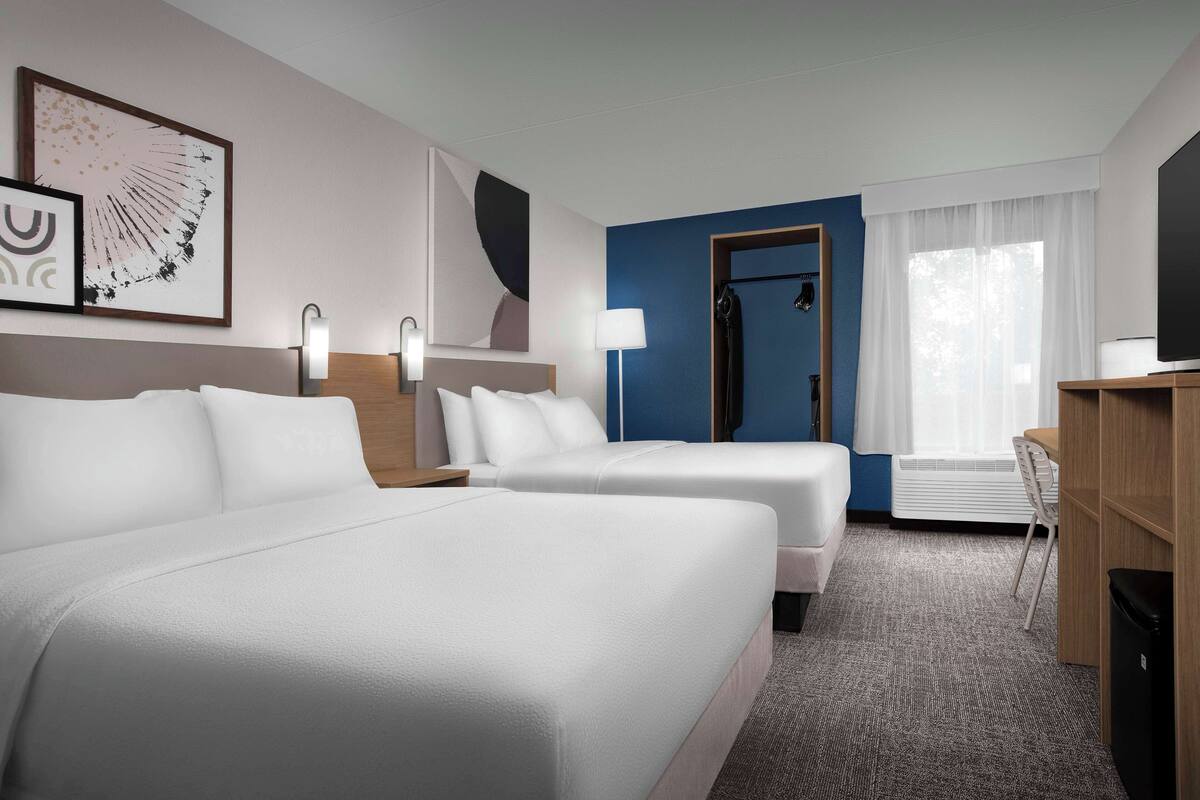 A hotel room with two beds, a desk, a chair, a TV, and a bathroom with a shower.