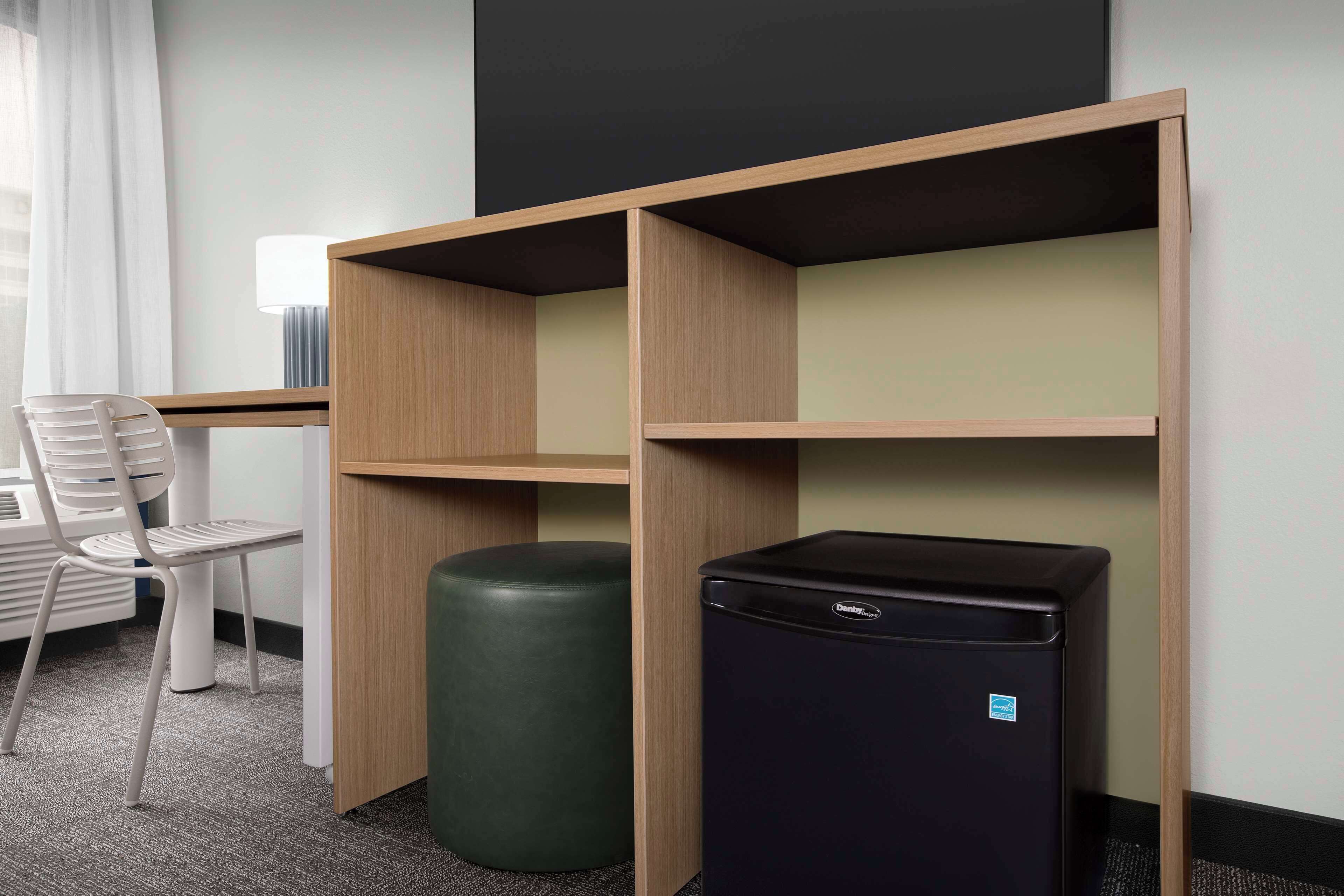 Une chambre d’hôtel équipée d’un bureau, d’une chaise et d’un réfrigérateur noir.