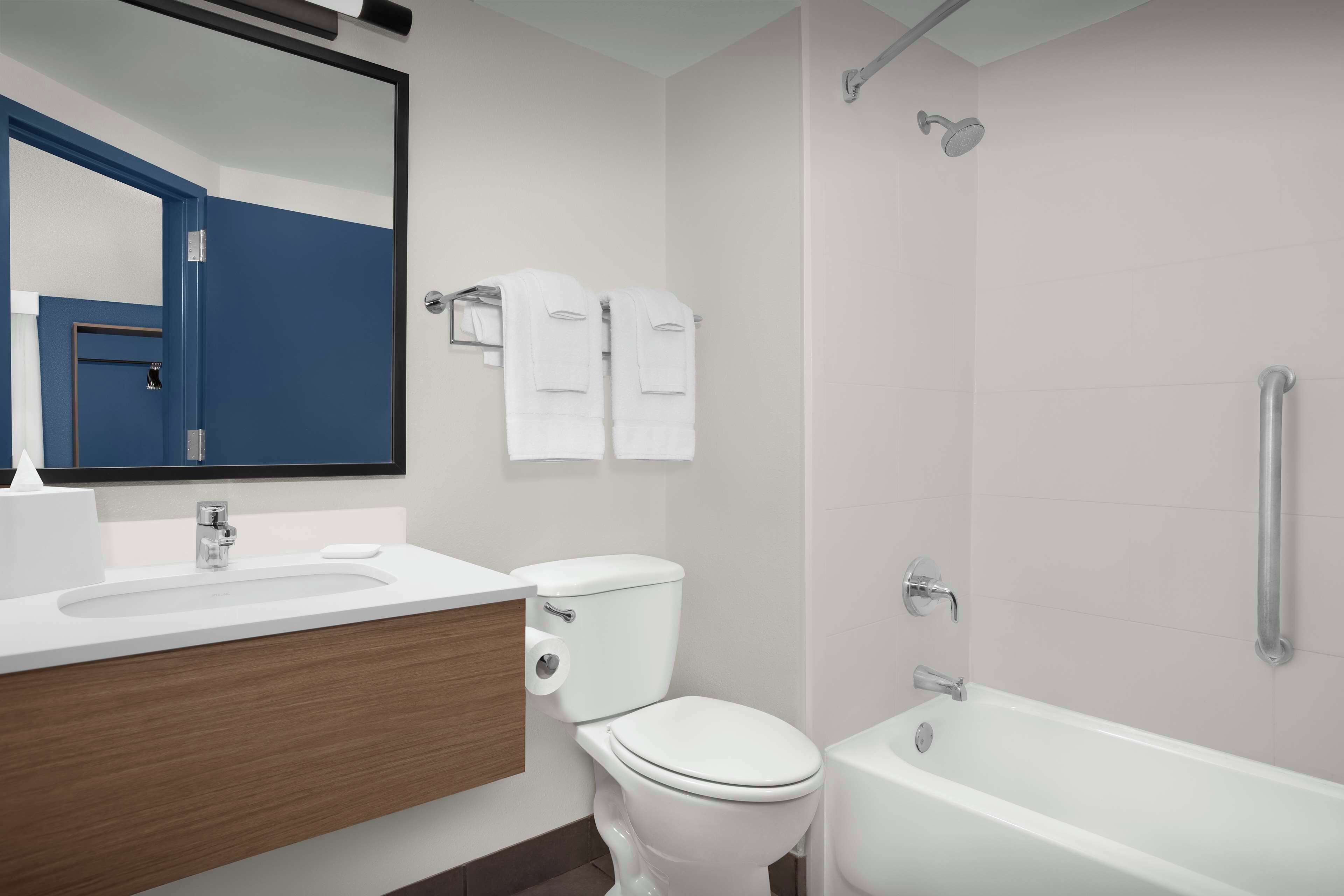 A modern bathroom with a white sink, toilet, and bathtub. There are two white towels hanging on a rack.