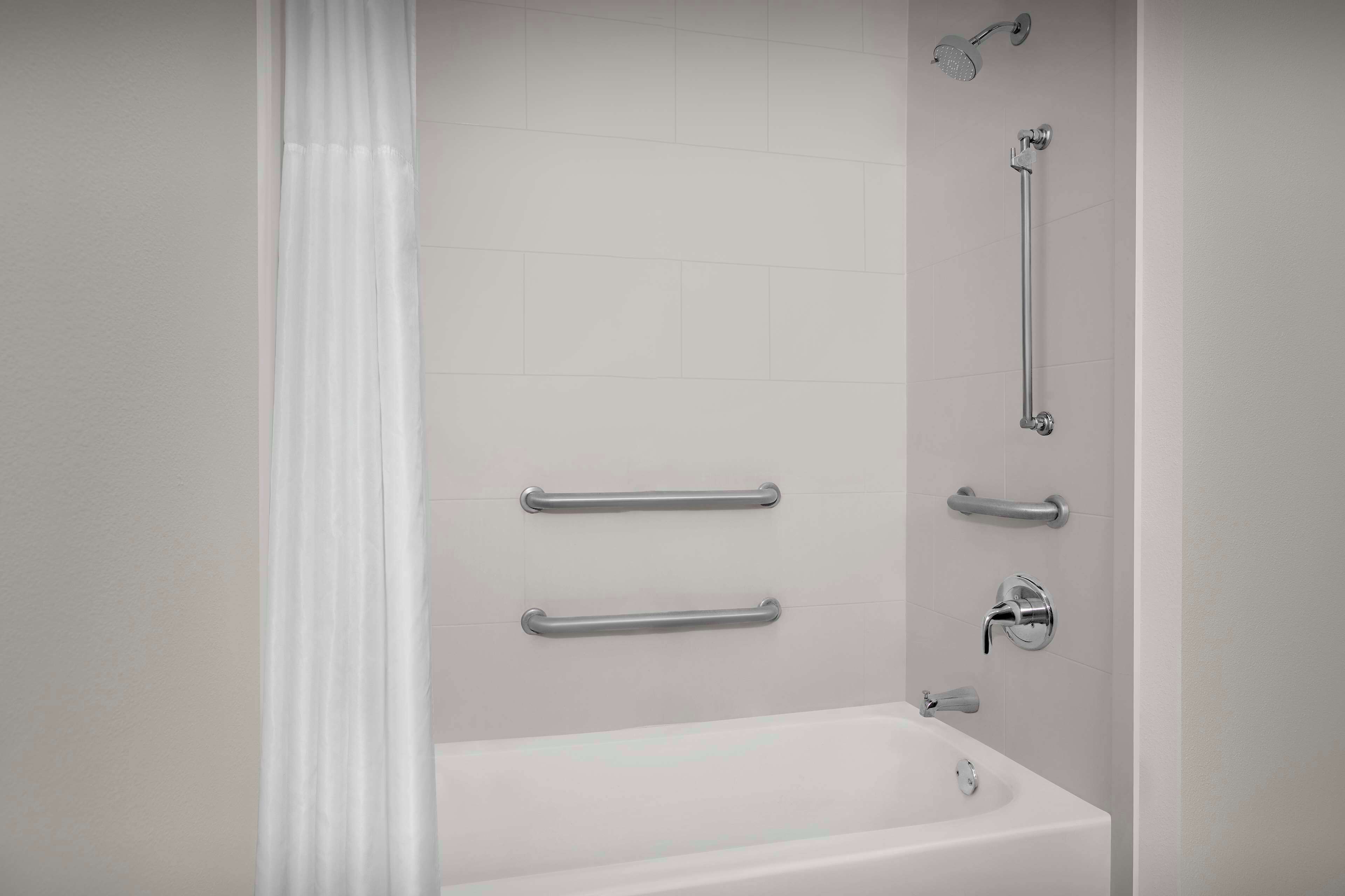 A bathroom with a bathtub, a shower, and grab bars.