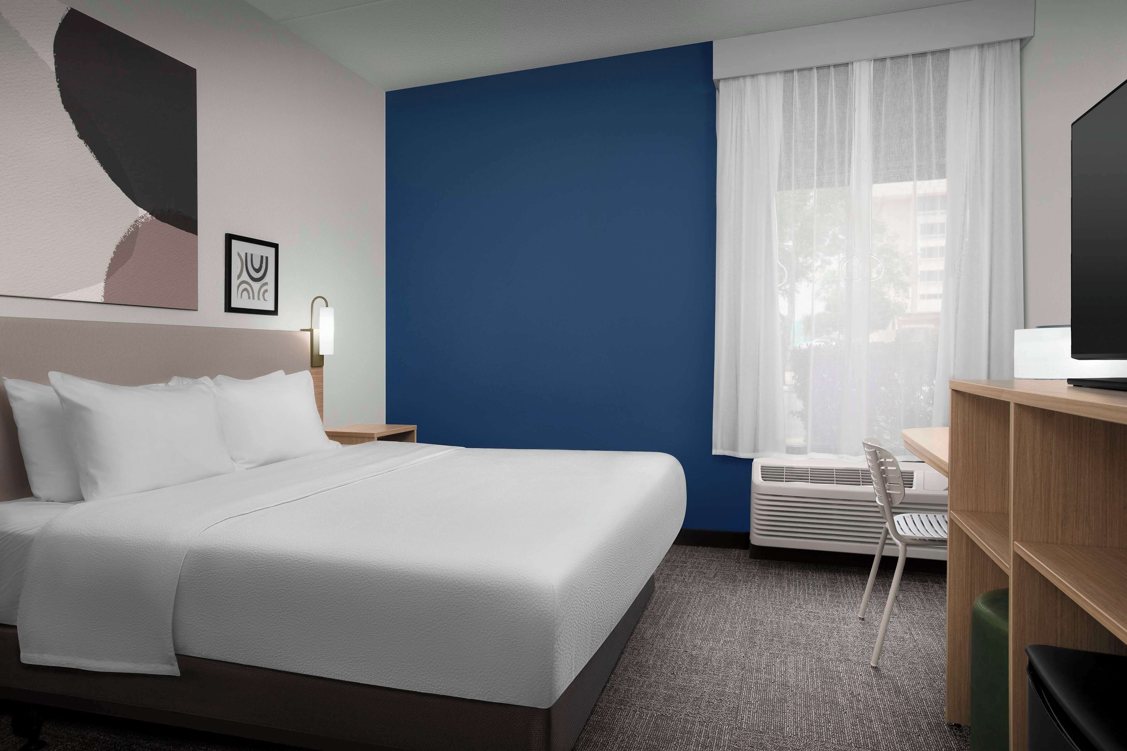 A hotel room with a bed, a desk, a chair, a TV, and a window with curtains.