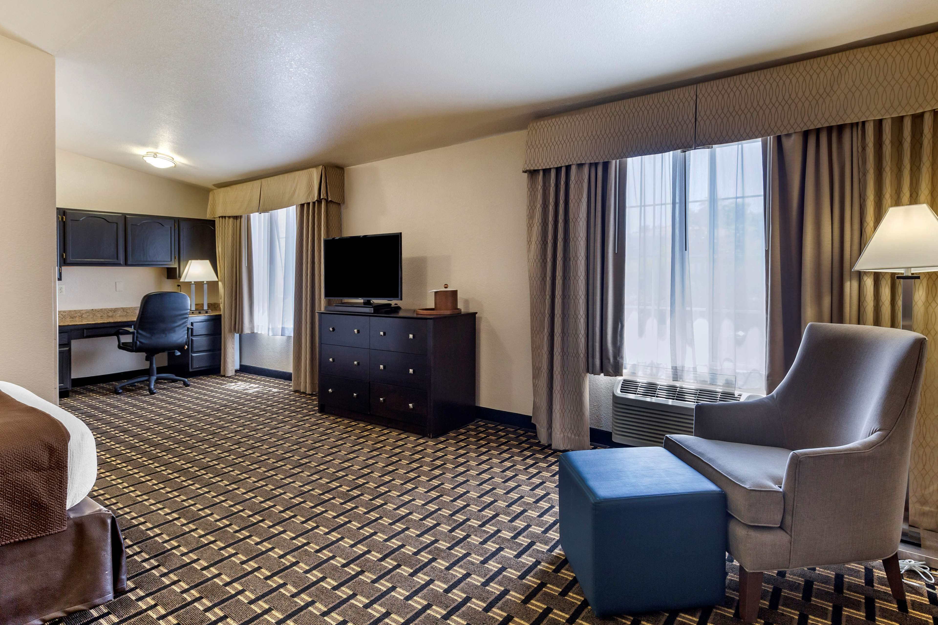 Ein Hotelzimmer mit einem Bett, einem Schreibtisch mit Stuhl, einem Fernseher, einer Kommode und einem großen Fenster mit Vorhängen.