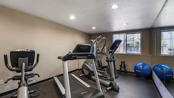 A gym with a treadmill, elliptical, and exercise balls.