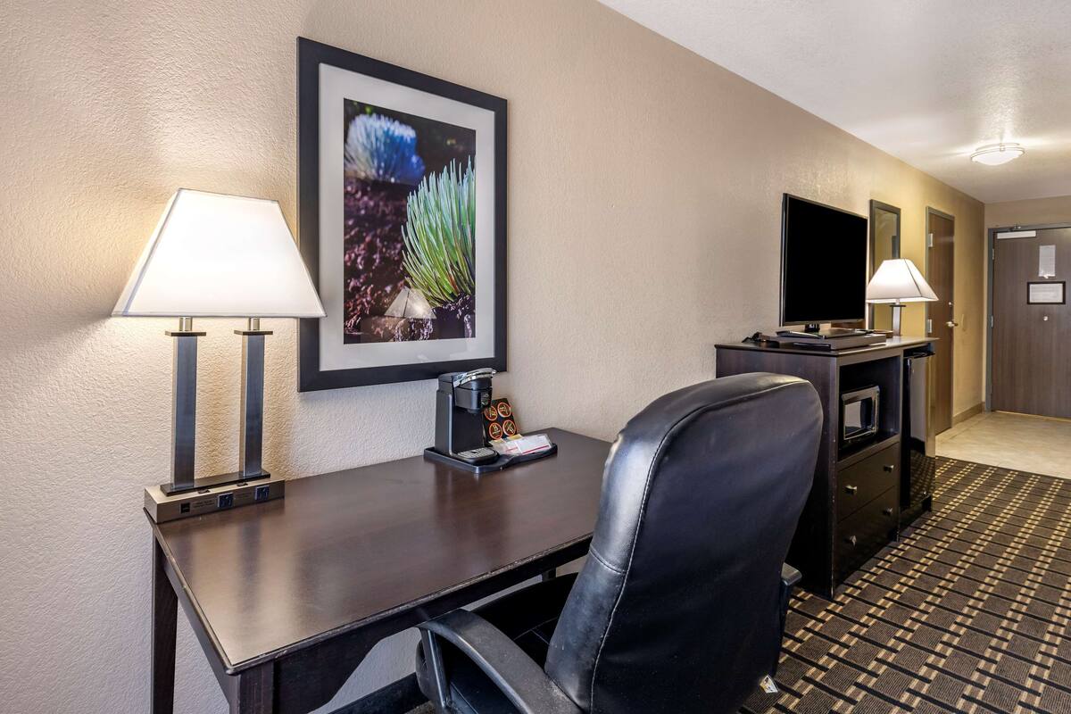 Ein Hotelzimmer mit Schreibtisch, zwei Lampen, einem Fernseher, einer Kaffeemaschine und einem gerahmten Bild an der Wand.