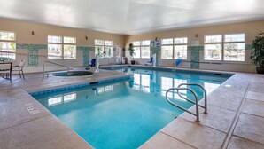 Une piscine intérieure à l’eau claire, avec des murs carrelés et une pièce baignée de lumière naturelle grâce à de grandes fenêtres.