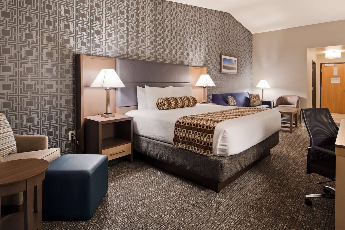 Ein Hotelzimmer mit einem großen Bett, zwei Nachttischen inklusive Lampen, einem Schreibtisch mit Stuhl, einem Sofa und einem Fernseher.