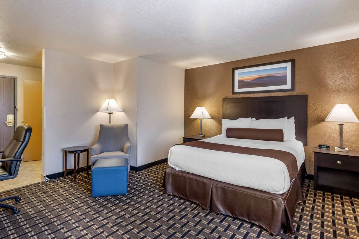 Ein Hotelzimmer mit einem großen Bett, zwei Sesseln, einem kleinen Tisch und einem Nachttisch mit einer Lampe.