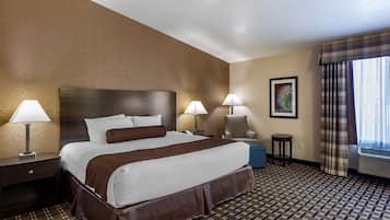 Una habitación de hotel con una cama grande, dos lámparas de noche, una silla, una mesita y una ventana con cortinas.