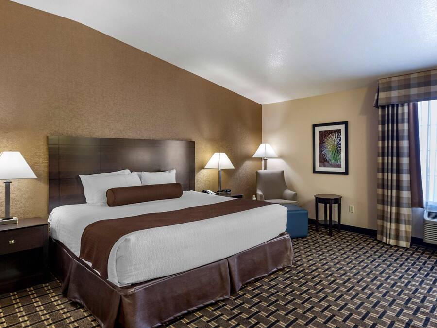 Una habitación de hotel con una cama grande, dos lámparas de noche, una silla, una mesita y una ventana con cortinas.