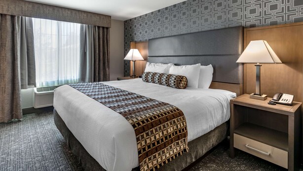 Une chambre d’hôtel avec un grand lit, deux tables de chevet avec des lampes, un mur à motifs et une fenêtre avec des rideaux.