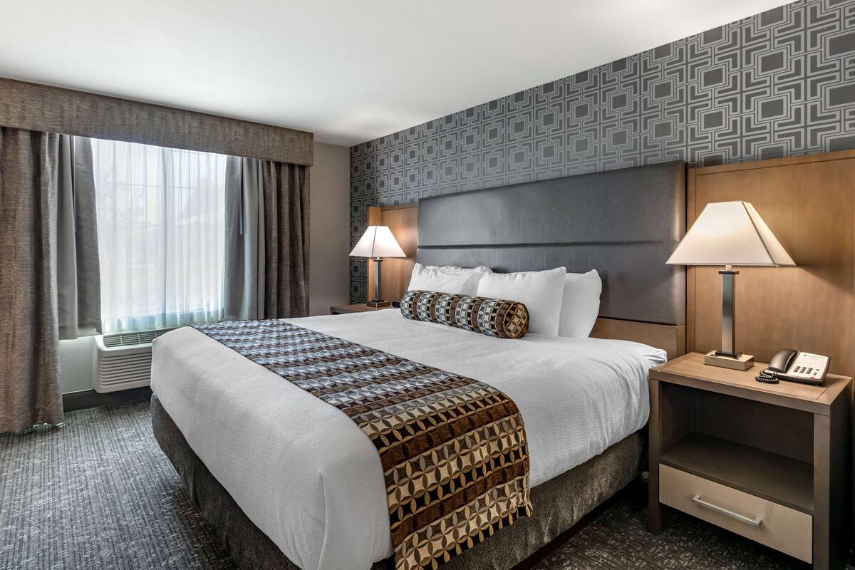 Ein Hotelzimmer mit einem großen Bett, zwei Nachttischen mit Lampen, einer Wand mit Muster und einem Fenster mit Vorhängen.