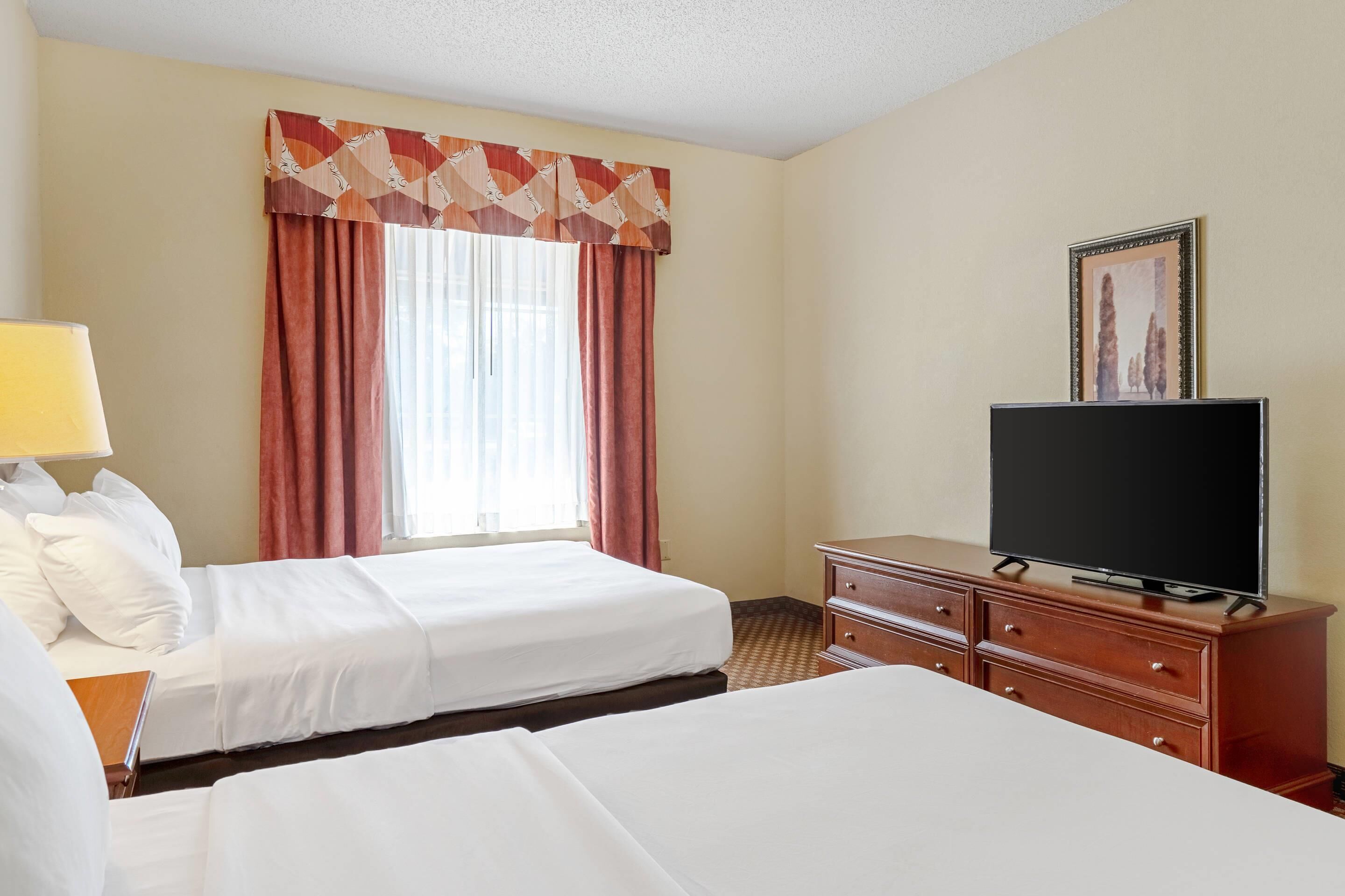 A hotel room with two beds, a television on a dresser, and a window with curtains.