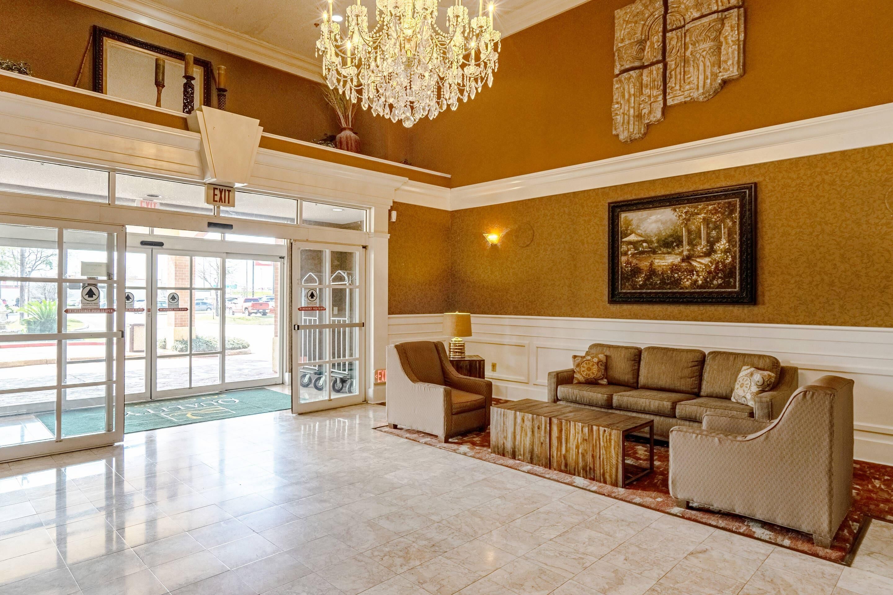 A spacious lobby with a chandelier, a sofa set, and a framed painting on the wall.
