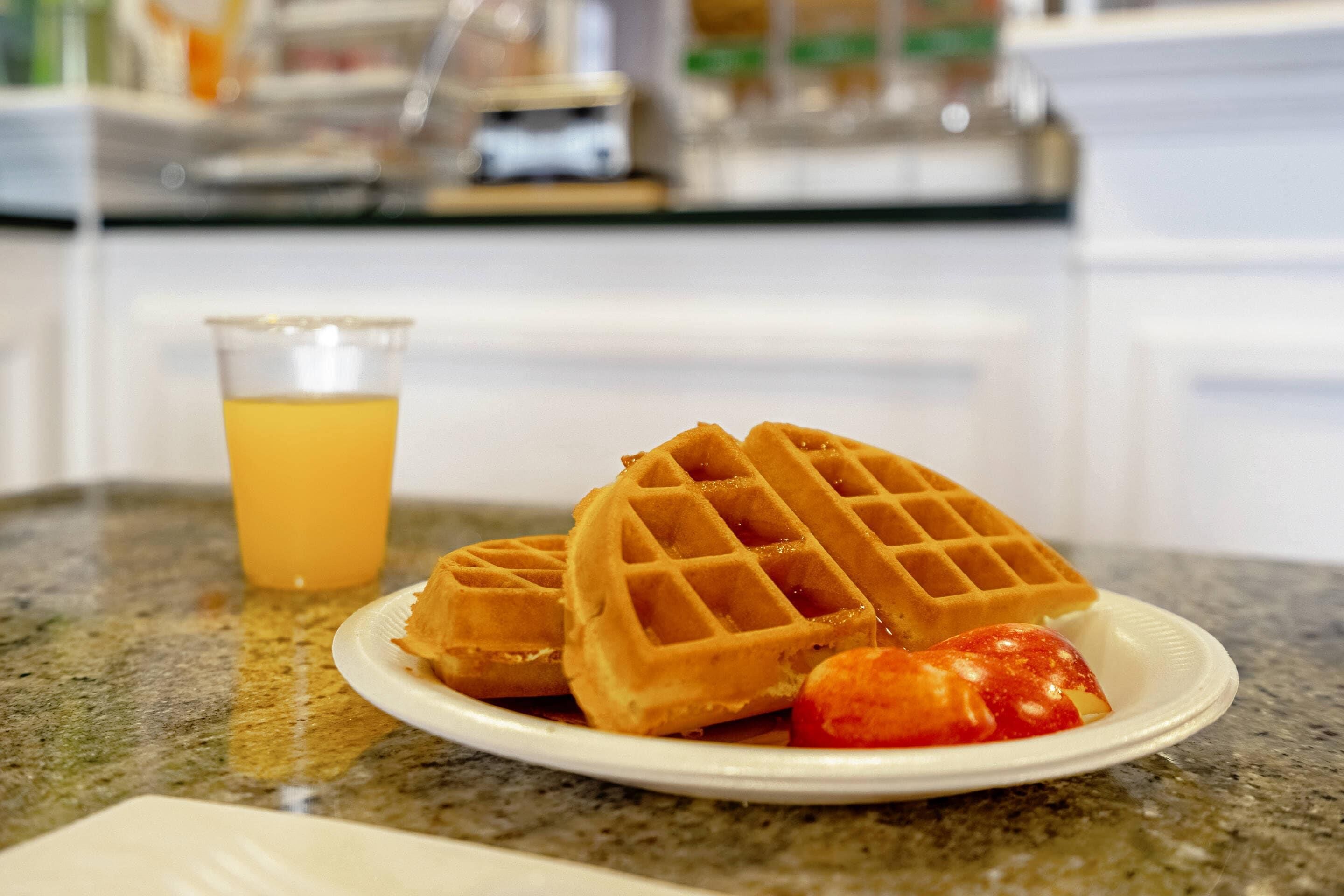 A plate with waffles and a glass of orange juice on a granite countertop.